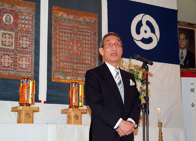 曼荼羅と双寳木の前で挨拶する祝主