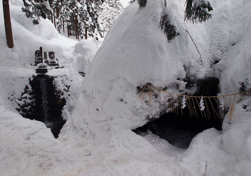 雪に閉ざされた里宮不動滝(左)と泰賢行者の霊窟(右)